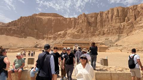       Tourists walking toward Hatshepsut Temple beneath desert cliffs
  