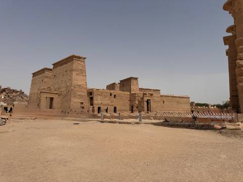       Wide view of a sandy courtyard with ancient stone temple buildings under a hazy sky
  