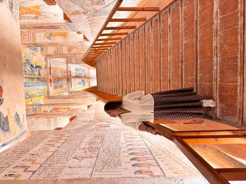       Woman looks up at colourful hieroglyphic walls while standing on a terracotta staircase inside a tomb
  
