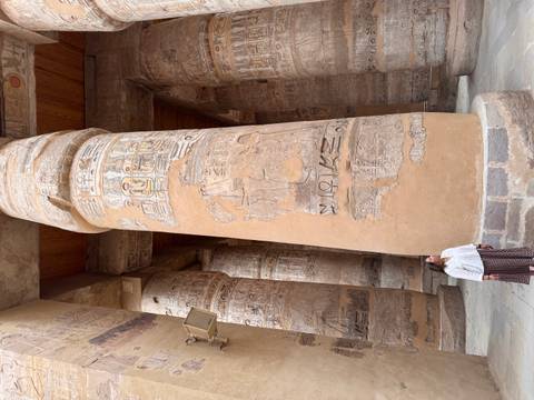      Visitor dwarfed by towering carved sandstone columns covered in hieroglyphs inside an Egyptian temple
  
