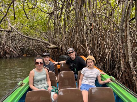       Family sits in a small boat surrounded by dense mangrove roots on a narrow waterway
  