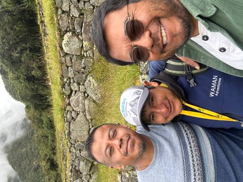       Three friends take a close selfie with stone terraces and misty mountains in the background.
  