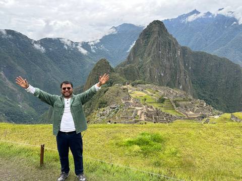       A smiling traveler raises his arms before the iconic ruins and peak of Machu Picchu.
  