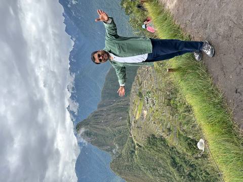       A traveler poses joyfully on a ledge overlooking Machu Picchu and cloud-capped Andes peaks.
  