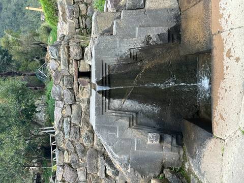       An ancient stone fountain pours clear water through an Inca-style carved channel.
  