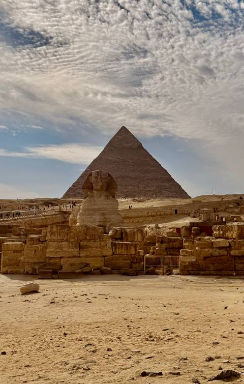       Great Pyramid of Giza rises behind the Sphinx under partly cloudy skies.
  