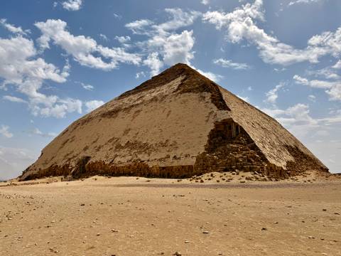       Distinctive Bent Pyramid rises from desert sands under a bright sky.
  