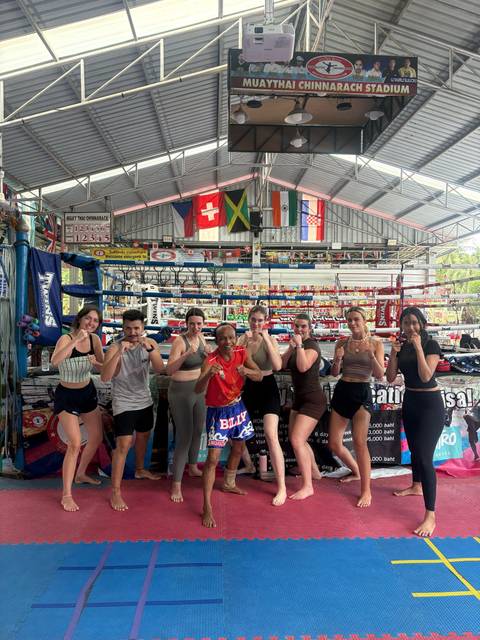       Travelers pose in fighting stances inside a colorful Muay Thai boxing gym.
  