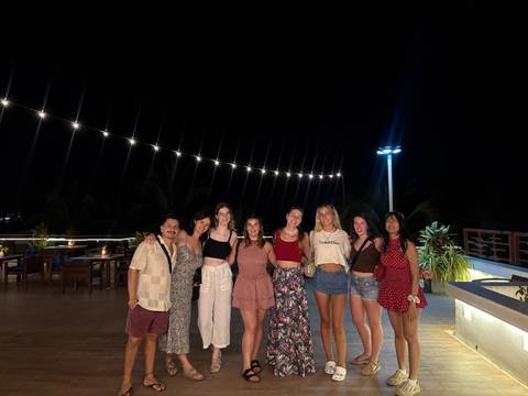       Group of friends dressed for a night out pose under string lights on a rooftop bar.
  