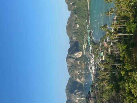       High viewpoint overlooks twin turquoise bays and jungle-covered limestone cliffs on a sunny morning.
  