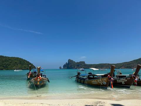       Colorful long-tail boats float on crystal-clear turquoise water with limestone islands in the distance.
  