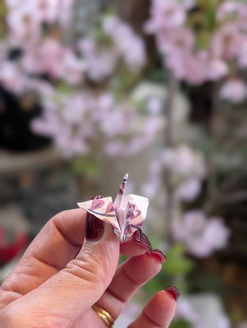       Hand holding a tiny patterned origami crane with soft floral background
  