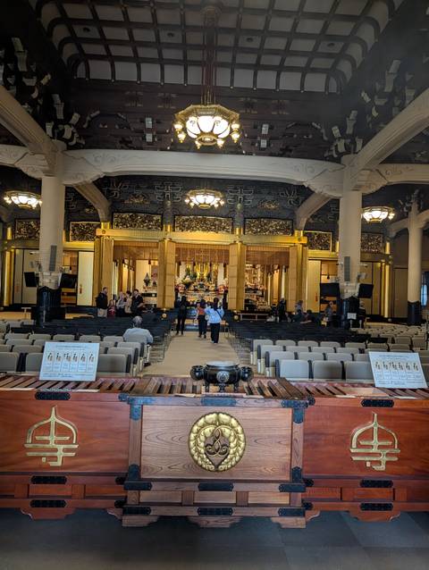       Interior of a large Buddhist hall with visitors seated before an ornate altar
  