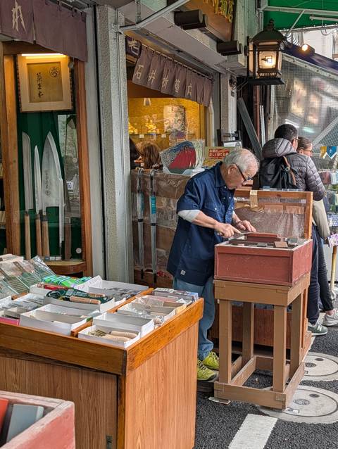       Craftsman sharpening knives on a whetstone outside a traditional shop
  