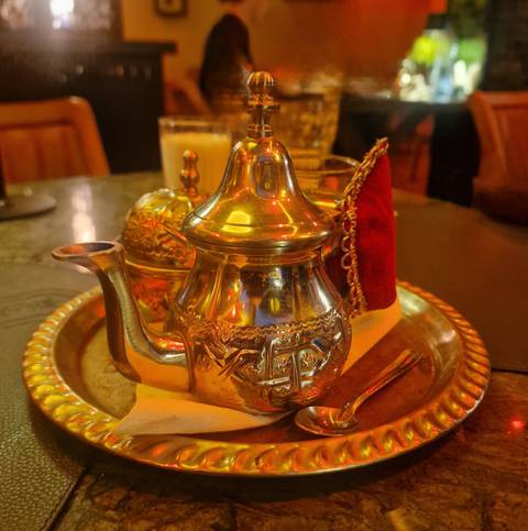       Traditional Moroccan silver teapot and cups on ornate brass tray under warm ambient lighting
  