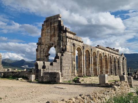       Impressive row of stone arches from the ancient Roman ruins at Volubilis under a bright sky
  