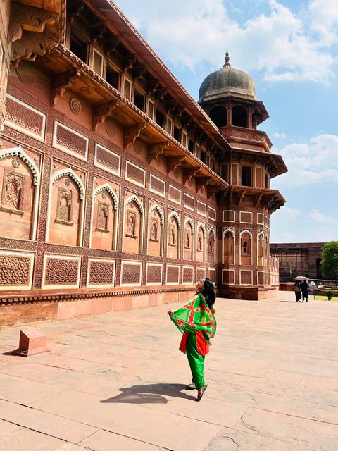       Woman gazing up at the ornate red-sandstone walls and carved niches of Agra Fort on a sunny day
  