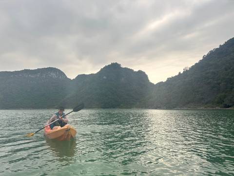       Person paddling a yellow kayak on emerald waters surrounded by towering limestone islands under soft light
  