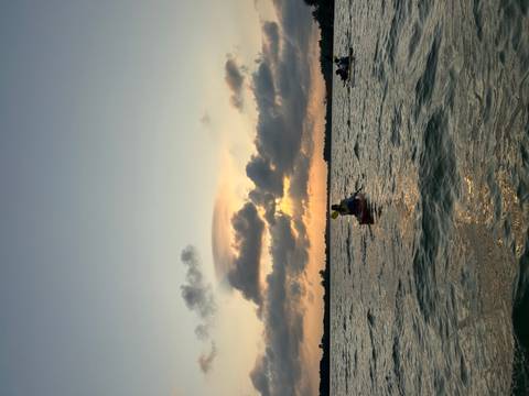       Kayakers silhouetted against a dramatic sunset over rippling water and distant clouds
  