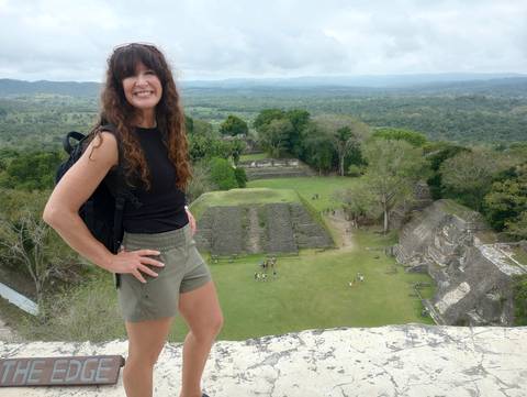       Woman posing atop a Maya pyramid with expansive jungle and plaza below at Xunantunich
  