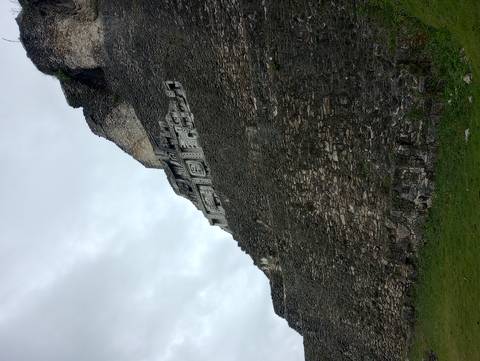       Stone face of the El Castillo temple showing intricate Maya carvings against a grey sky
  