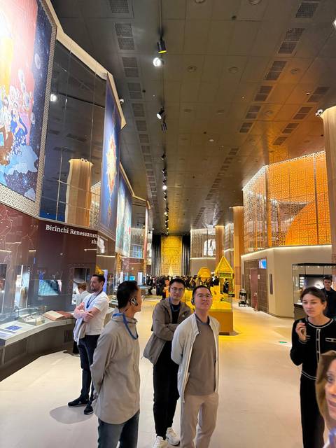       Visitors explore a modern, brightly lit museum hall with ornate decorative panels and exhibits.
  
