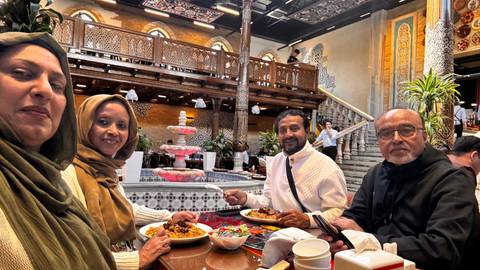       Four diners smile around a table laden with Uzbek dishes in a richly decorated restaurant interior.
  