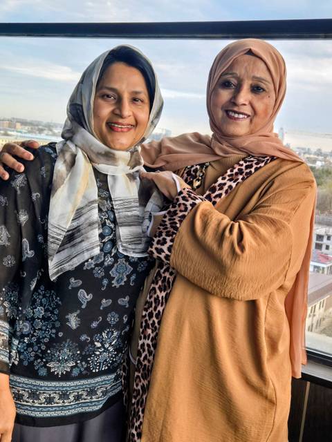       Close-up of two women in patterned hijabs and shawls embracing and smiling.
  