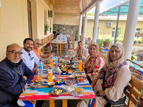       A family group shares a colorful outdoor meal with traditional Uzbek dishes and drinks.
  