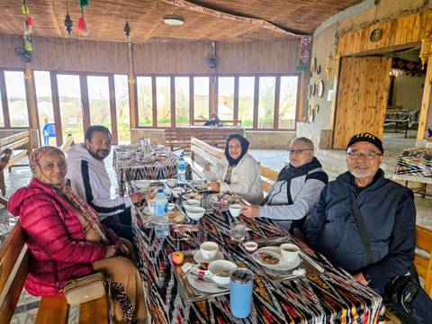       Travellers enjoy a rustic meal at long tables inside a wooden lodge with panoramic windows.
  