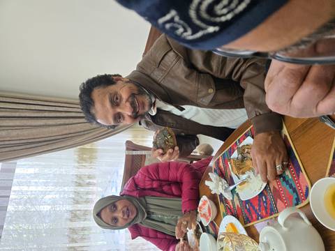       A man shows a piece of local cuisine while seated at a wooden dining table.
  