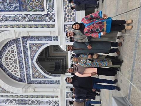       Six travellers in colorful clothing stand outside a blue-tile mosque entrance.
  
