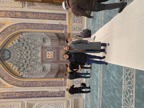       Two men pose inside a richly decorated blue-and-gold mosque prayer hall.
  
