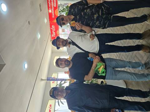       Four men in casual clothes smile while holding local pastries inside a bright shop.
  