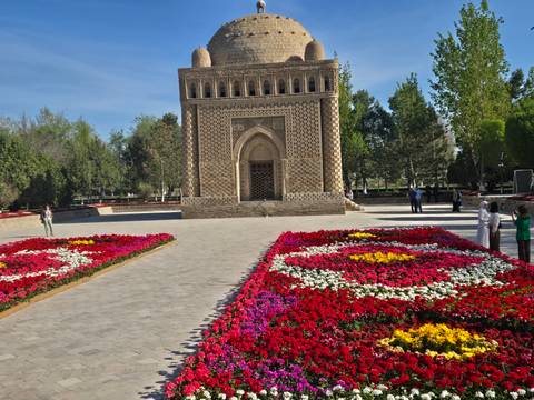       Vibrant geometric flower beds frame a ninth-century brick mausoleum set in a manicured park.
  