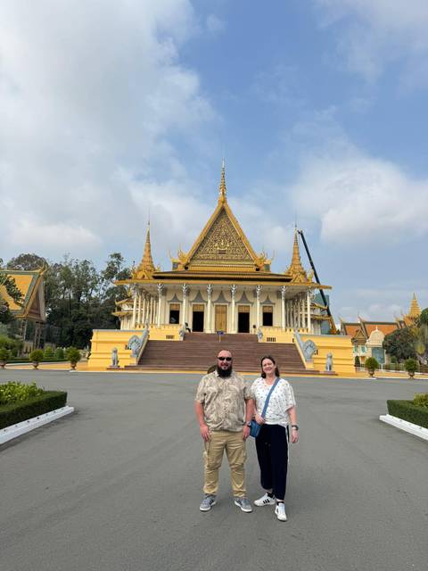      Two travellers pose before the ornate yellow Throne Hall of the Royal Palace in Phnom Penh.
  