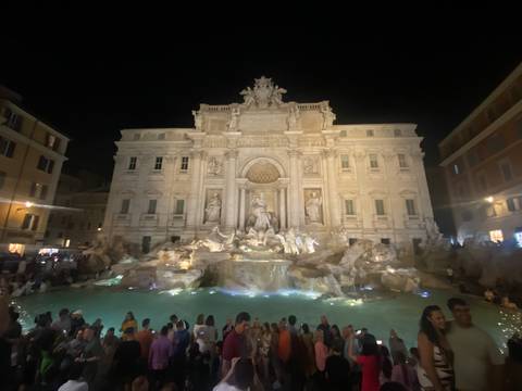       Night view of the illuminated Trevi Fountain with crowds gathered around the basin
  