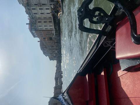       View from inside a gondola gliding along a shimmering Venetian canal beneath sunny skies
  