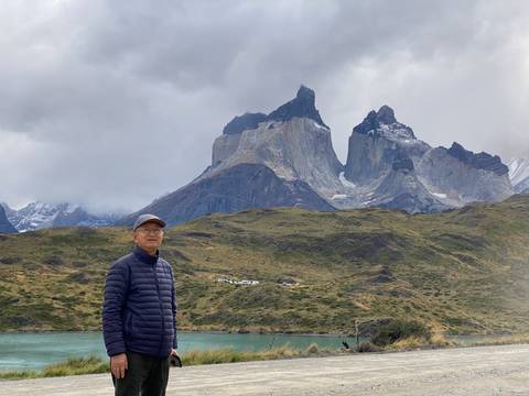       Traveler stands in front of the dramatic Cuernos del Paine rock formations under swirling clouds.
  