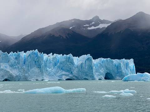       Jagged ice spires of Perito Moreno Glacier towering over a milky-green lake with misty mountains beyond.
  