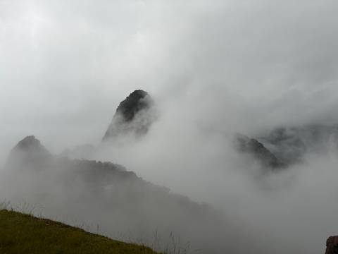       Heavy fog obscures the iconic peak of Huayna Picchu and surrounding mountains, with ruins barely visible.
  