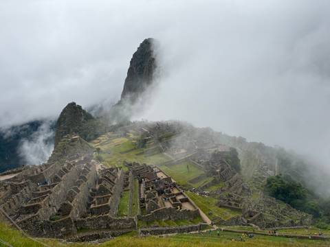       Classic postcard panorama of Machu Picchu with Huayna Picchu peak looming behind under drifting cloud.
  