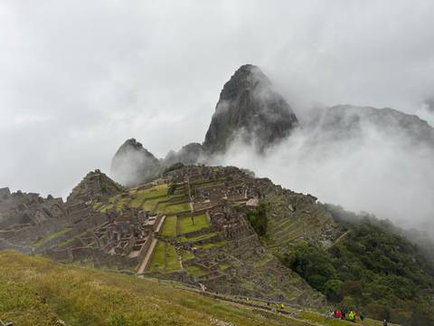       Stone ruins and terraces of Machu Picchu framed by swirling clouds with iconic peaks behind.
  
