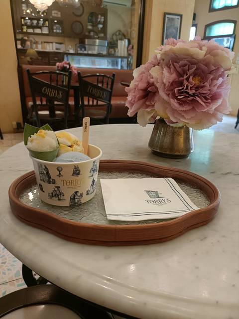      A cup of artisan ice cream on a wooden tray in a stylish café, with flowers and branded napkin.
  