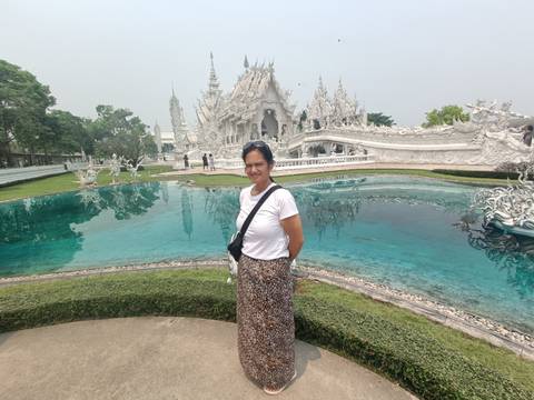       Visitor poses beside the reflective pond at Chiang Rai’s striking white temple, Wat Rong Khun.
  