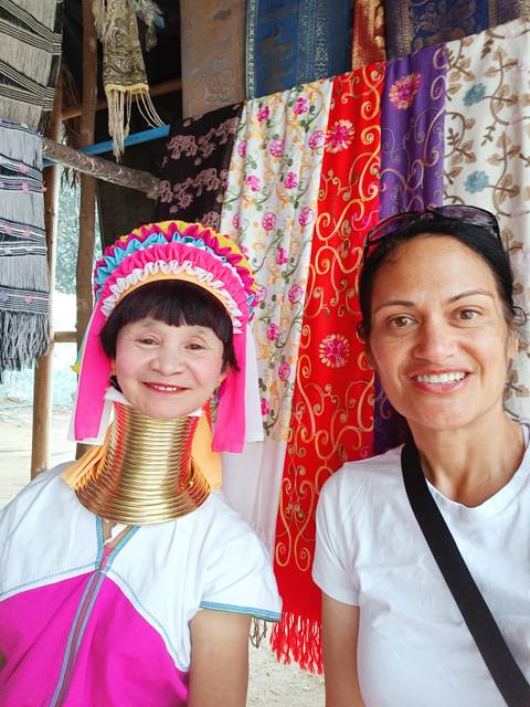       Tourist poses with a traditionally dressed long-neck Karen woman in a colorful market stall.
  