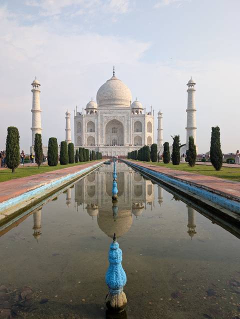       Iconic Taj Mahal reflected perfectly in its long central pool with manicured gardens on a calm day
  