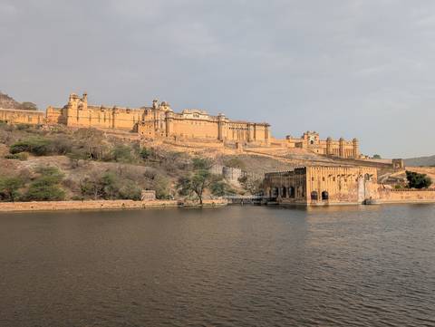       Panoramic view of the honey-colored Amber Fort sprawling along a ridge beside a calm lake
  