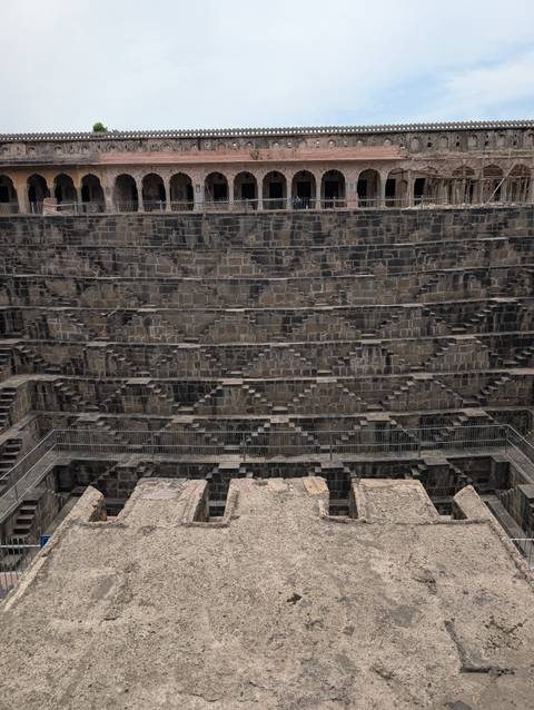       Symmetrical stone steps forming a deep geometric stepwell pattern viewed head-on
  