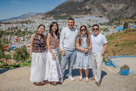       Group of five travellers posing with the blue-painted hillside town of Chefchaouen in the background
  